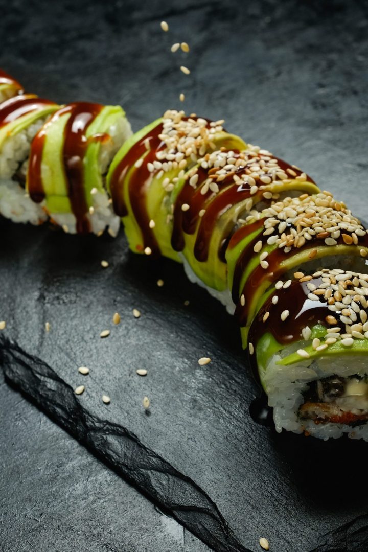 Green dragon avocado sushi rolls on dark background with sesame seeds sprinkled from above. Creative food photography art.